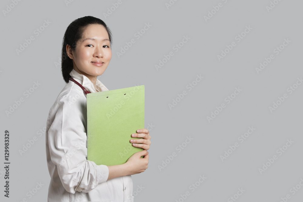 Portrait of a confident Asian female doctor holding clipboard over gray background Portrait of a confident Asian female doctor holding clipboard over gray background