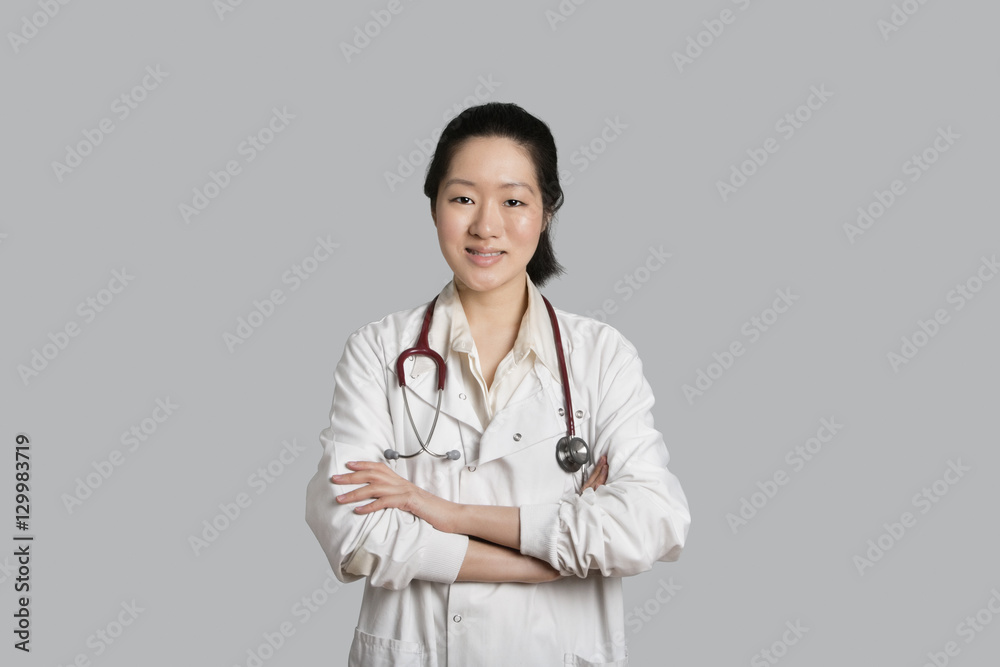Portrait of an Asian female doctor standing with arms crossed over gray background Portrait of an Asian female doctor standing with arms crossed over gray background