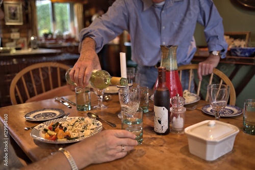 Man in blue shirt pouring white wine to glass during dinner