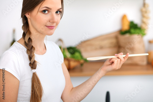 Young woman is cooking in a kitchen. Housewife is tasting the soup by wooden spoon