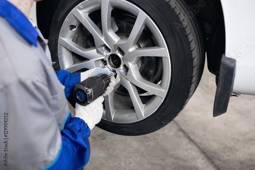 car mechanic screwing or unscrewing  wheel of lifted automobile by pneumatic wrench at repair service station