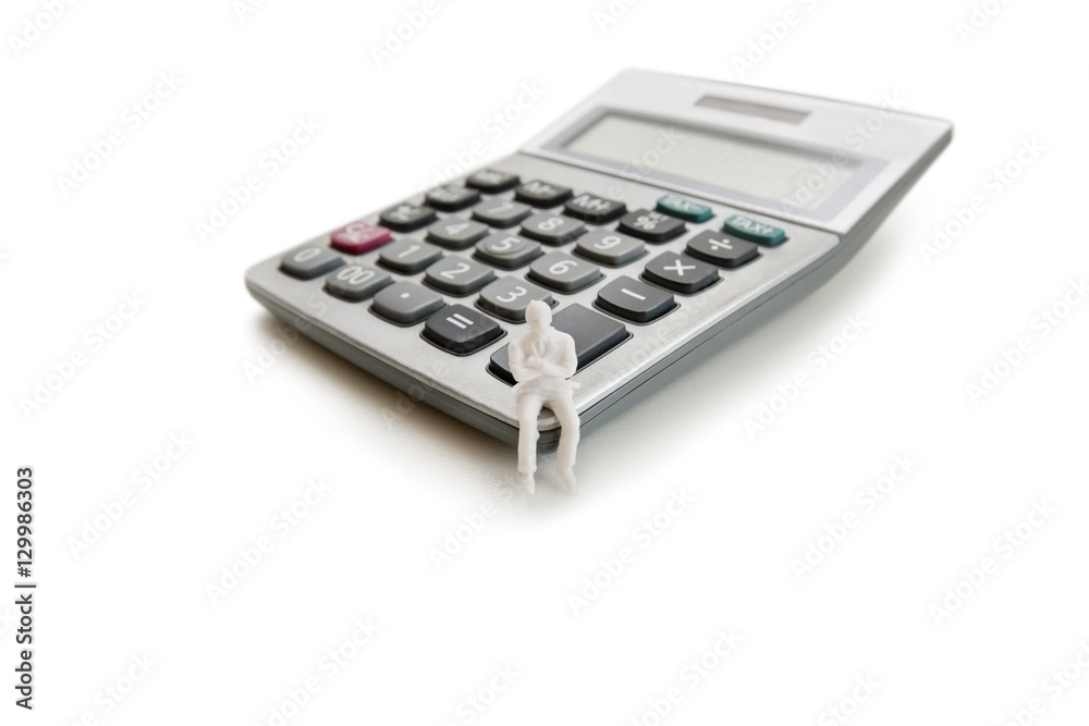 A small dummy figure sitting on a calculator over white background A small dummy figure sitting on a calculator over white background