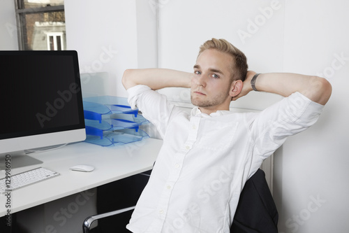 Portrait of young businessman relaxing on chair at office desk