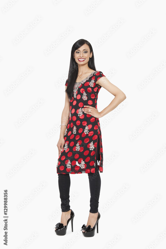 Full length portrait of Indian female in traditional wear standing with hand on hip over gray background Full length portrait of Indian female in traditional wear standing with hand on hip over gray background