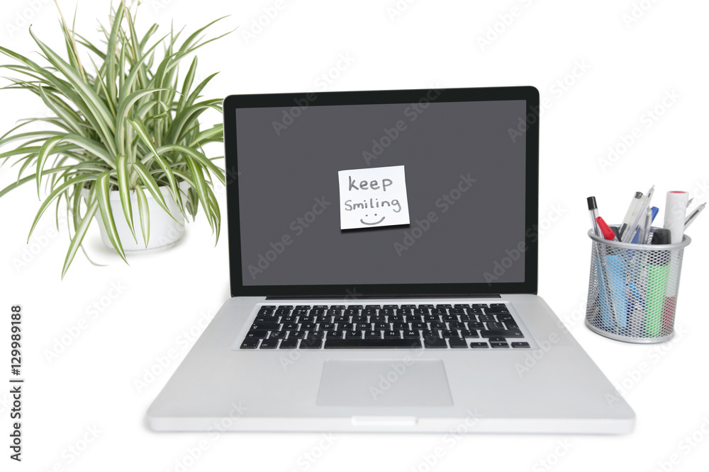 Smiley face sticky note on laptop with office supplies and pot plant Smiley face sticky note on laptop with office supplies and pot plant