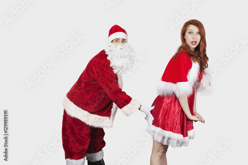 Portrait of Santa touching Mrs. Santa inappropriately against gray background