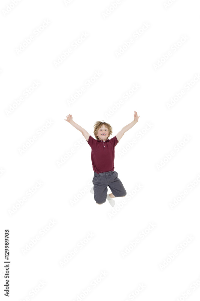 Portrait of elementary boy jumping in air with arms raised over white background