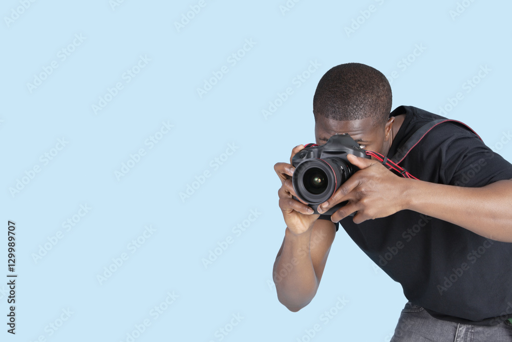 Young man taking photo through digital camera over blue background Young man taking photo through digital camera over blue background
