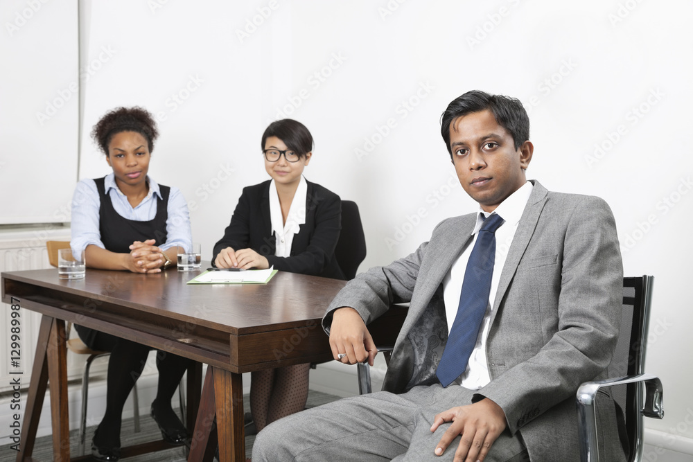 Portrait of Asian male with female colleagues in background at desk in office Portrait of Asian male with female colleagues in background at desk in office