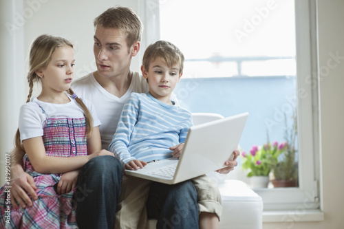 Father and children using laptop while sitting on chair