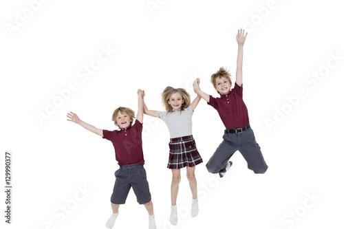 Portrait of happy school children holding hands while jumping over white background