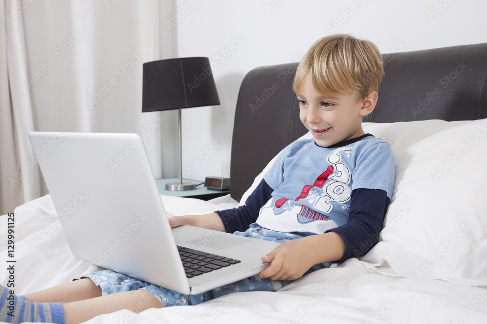 Smiling Caucasian boy using laptop computer in bed Smiling Caucasian boy using laptop computer in bed