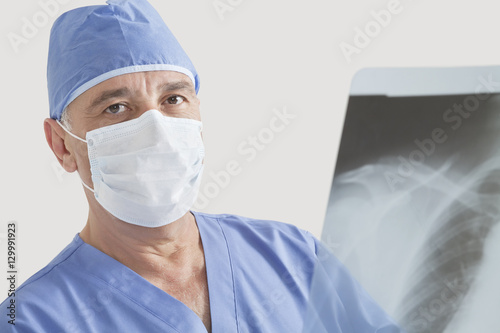 Portrait of senior male surgeon examining x-ray over gray background