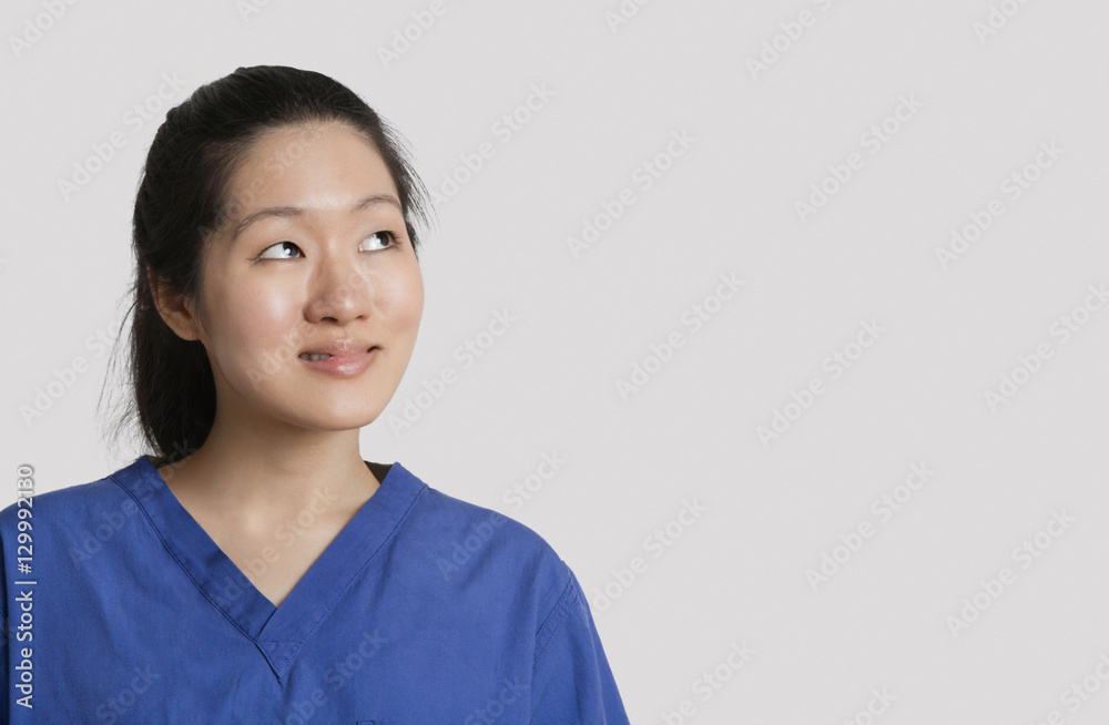 Young Asian female doctor looking up over gray background Young Asian female doctor looking up over gray background