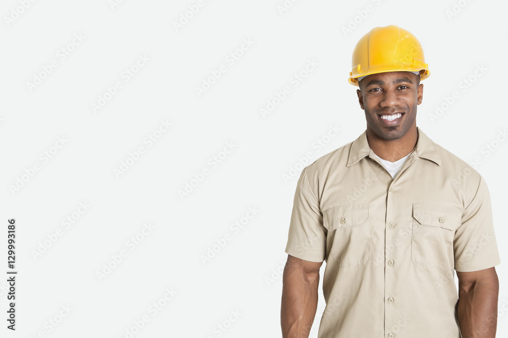 Portrait of happy young African man wearing yellow hard hat helmet over gray background