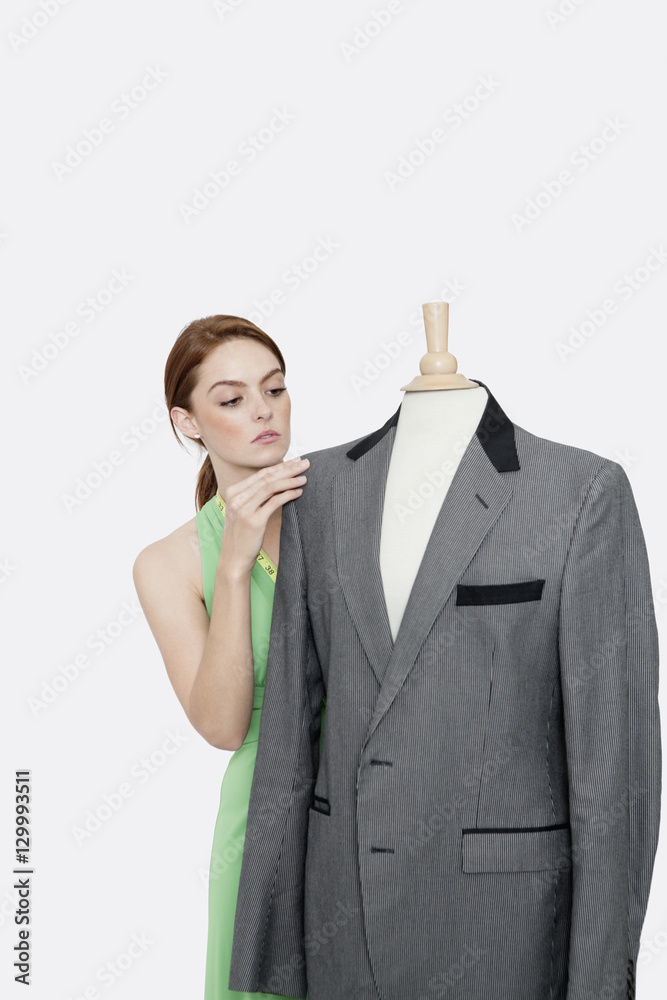 Young female fashion designer looking at blazer on tailor's dummy over gray background Young female fashion designer looking at blazer on tailor's dummy over gray background