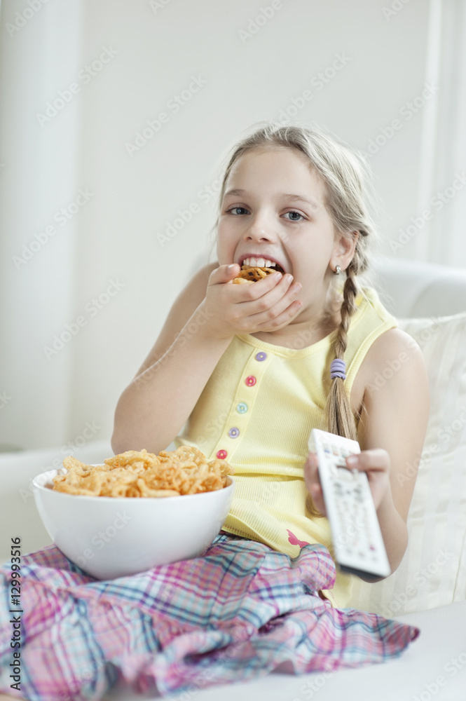 Girl watching TV as she stuffs her mouth with wheel shape snack pellets Girl watching TV as she stuffs her mouth with wheel shape snack pellets