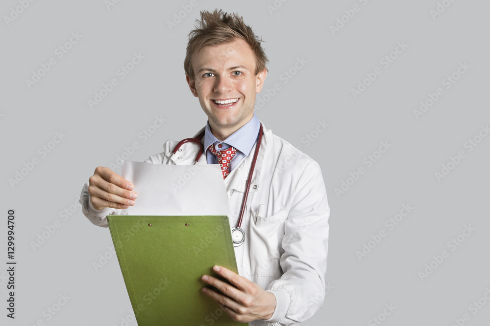 Portrait of a happy male doctor holding a clipboard over gray background Portrait of a happy male doctor holding a clipboard over gray background