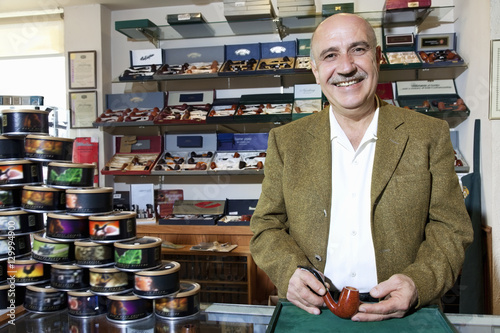 Portrait of a happy mature tobacco shop owner with cans on display photo
