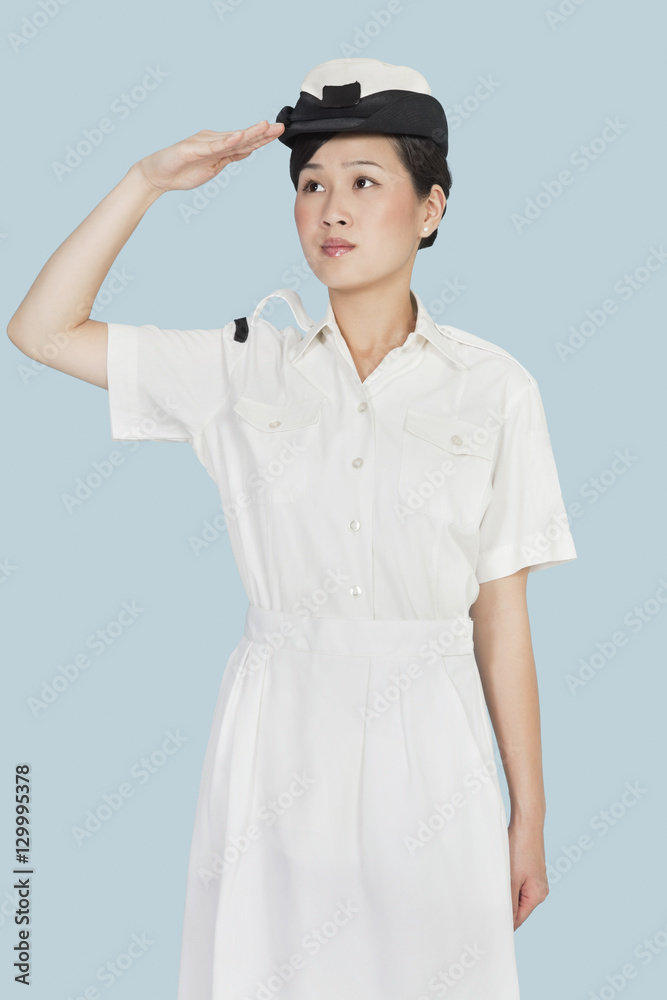 Beautiful young US Navy officer saluting over light blue background Beautiful young US Navy officer saluting over light blue background