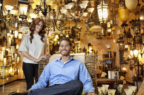 Portrait of handsome young man sitting while woman standing background in lights store