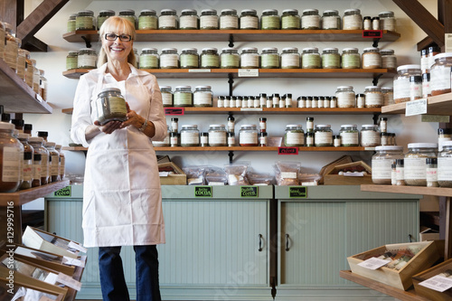 Portrait of a happy senior merchant standing with spice jar in store photo