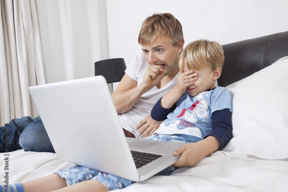Father and son watching scary movie on laptop in bed Father and son watching scary movie on laptop in bed