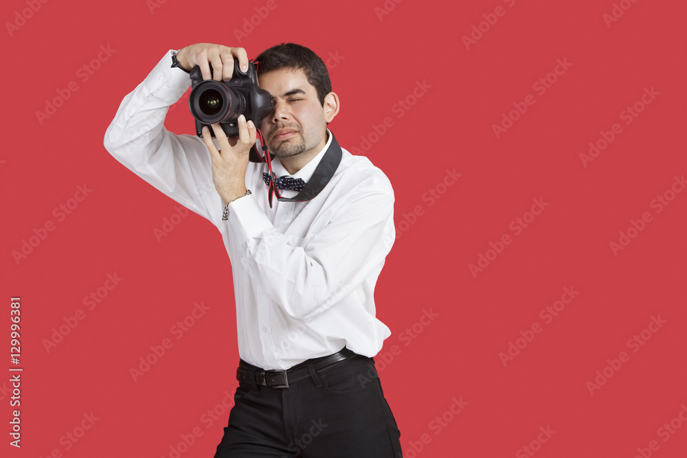 Mixed race man taking picture with digital camera over red background Mixed race man taking picture with digital camera over red background