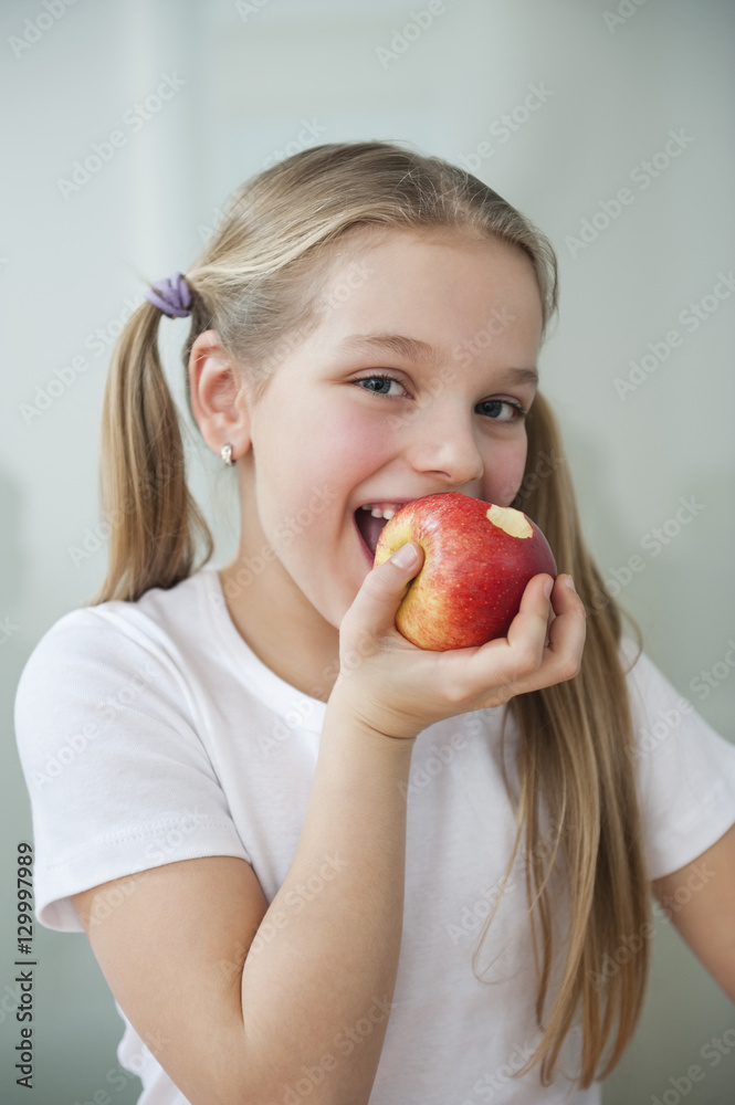 Portrait of happy young girl eating an apple over gray background Portrait of happy young girl eating an apple over gray background
