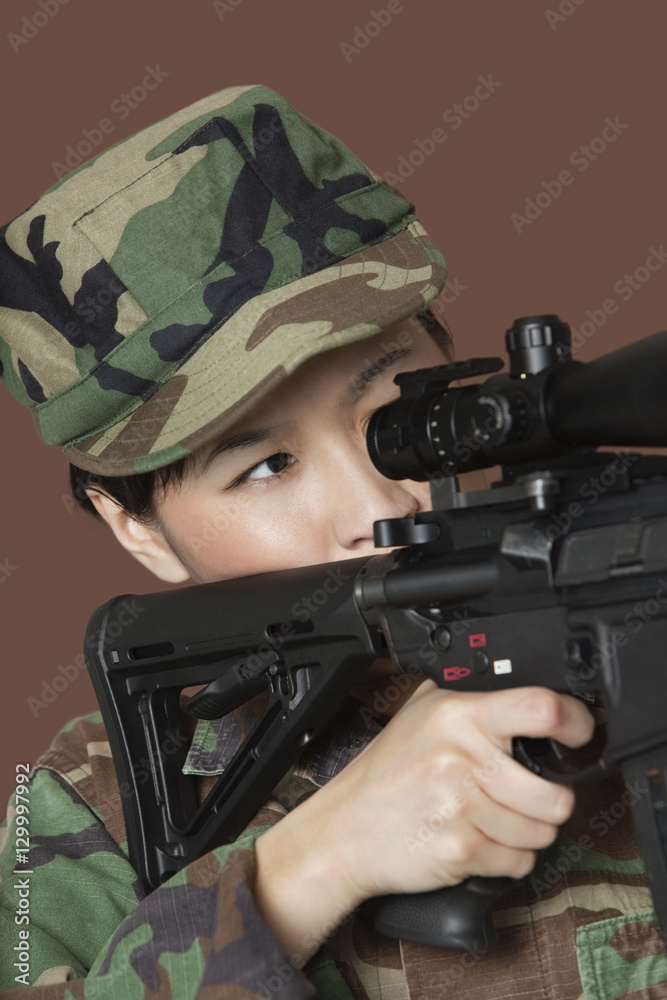 Young female US Marine Corps soldier aiming M4 assault rifle over brown background Young female US Marine Corps soldier aiming M4 assault rifle over brown background