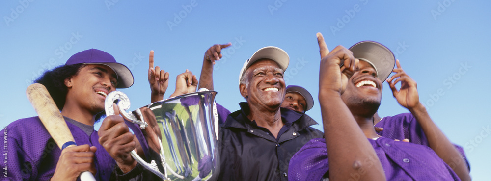 Obraz premium Panoramic shot of cheerful baseball players with trophy celebrating victory against clear sky