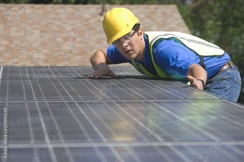 Young maintenance worker installing solar panels on rooftop