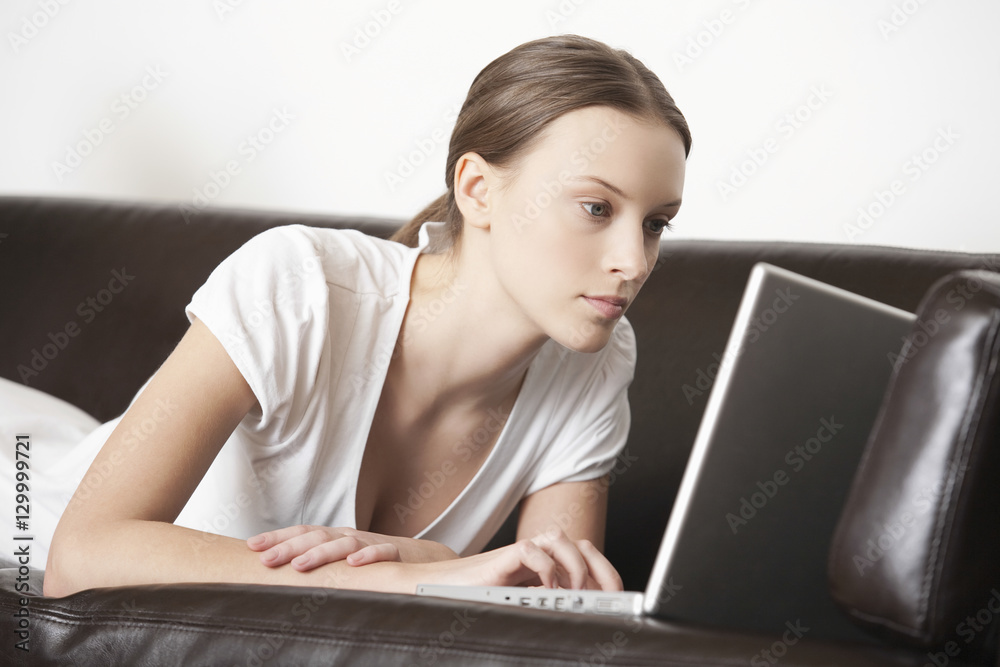 Young woman using laptop while lying on leather sofa Young woman using laptop while lying on leather sofa