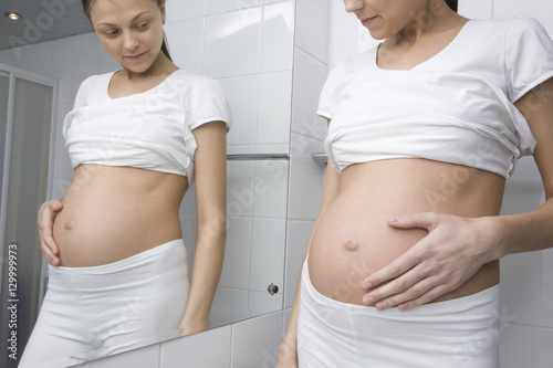 Midsection of pregnant young woman standing in front of bathroom mirror © moodboard