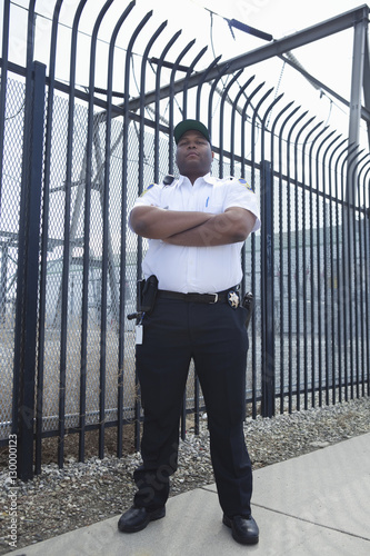 Confident security guard standing with arms crossed in front of the prison fence