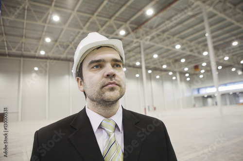 Confident young businessman wearing hardhat in brightly lit warehouse