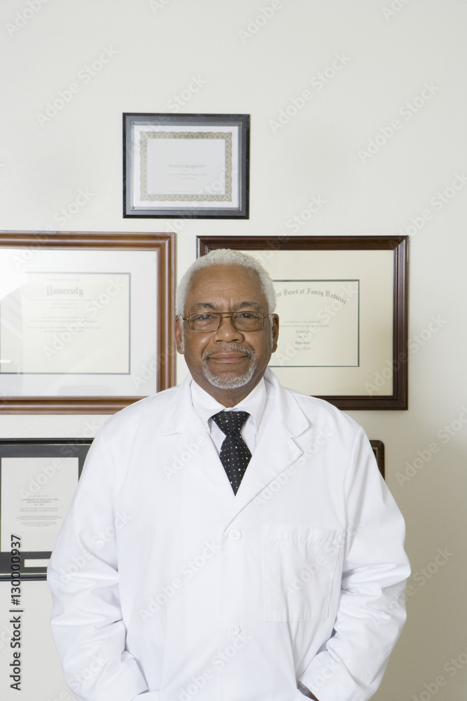 Portrait of a confident African American doctor with framed certificates hanging on wall