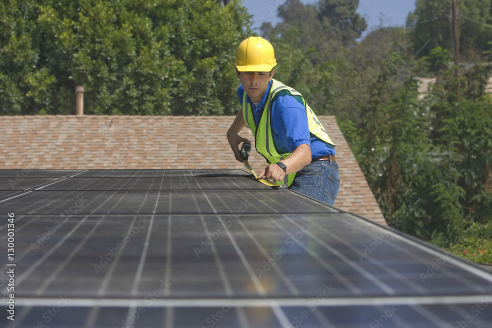 Young maintenance worker measuring solar panels on rooftop