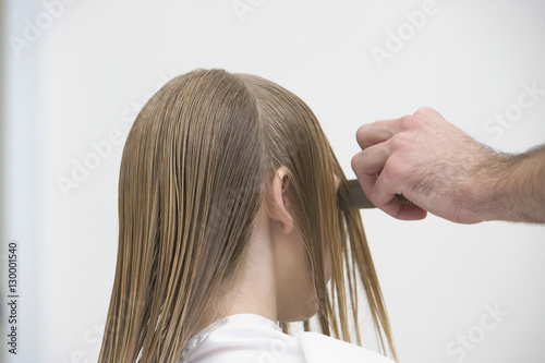 Cropped image of hairdresser's hand combing client's wet hair at beauty salon
