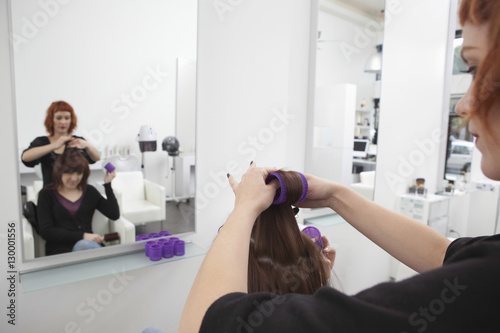 Female hairdresser rolling up curler for her client in salon