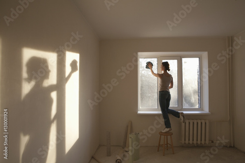 Full length rear view of young woman cleaning window in new apartment