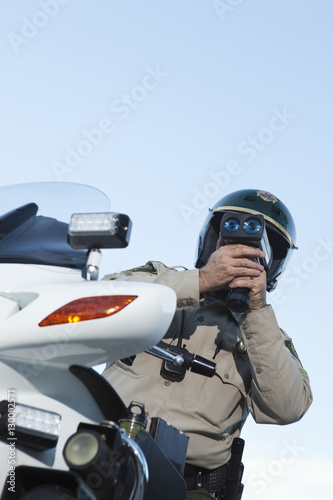 Low angle view of middle aged traffic cop monitoring speed through radar against sky