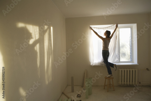 Fototapeta Naklejka Na Ścianę i Meble -  Full length rear view of young woman fitting curtain in new apartment