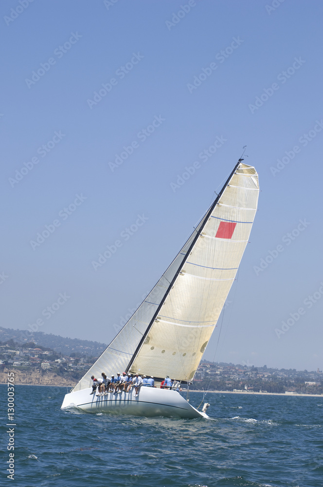Naklejka premium Group of crew members sitting on the side of a sailboat in the ocean