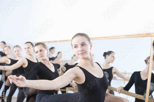Row of female ballet dancers practicing at barre in rehearsal room