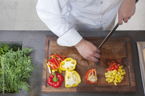 Billede på lærred Midsection of male chef dicing red and yellow bell peppers in commercial kitchen