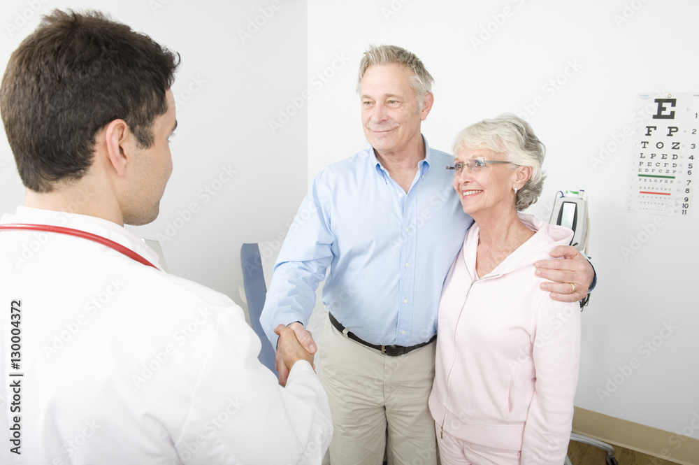 Obraz premium A thankful senior male besides wife shaking hands with the doctor in clinic