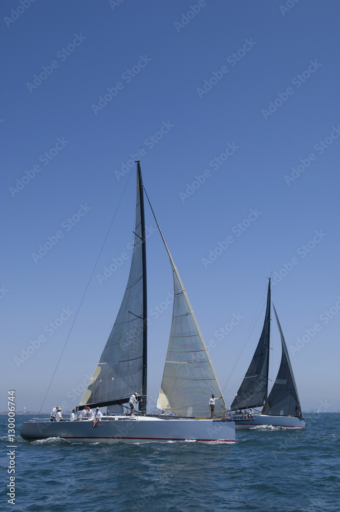 Overview of sailboats racing in the blue and calm ocean against sky