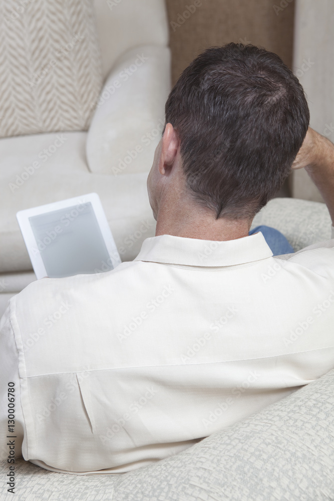Rear view of man with digital tablet sitting on sofa at home Rear view of man with digital tablet sitting on sofa at home
