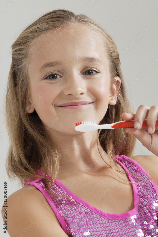 Portrait of young girl holding toothbrush against gray background Portrait of young girl holding toothbrush against gray background